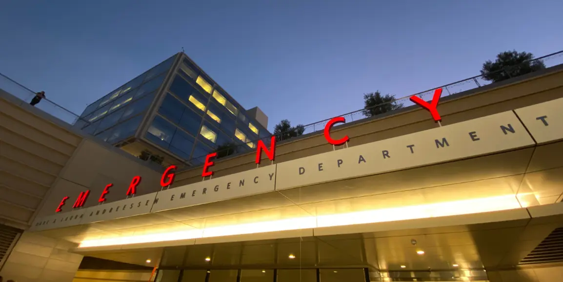 The Stanford Emergency Department entrance at dusk, its cardinal-red EMERGENCY sign glowing beneath a twilight sky.